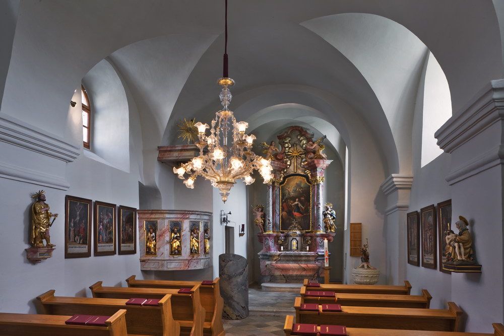 Interior view of a baroque church with altar, paintings and a chandelier.