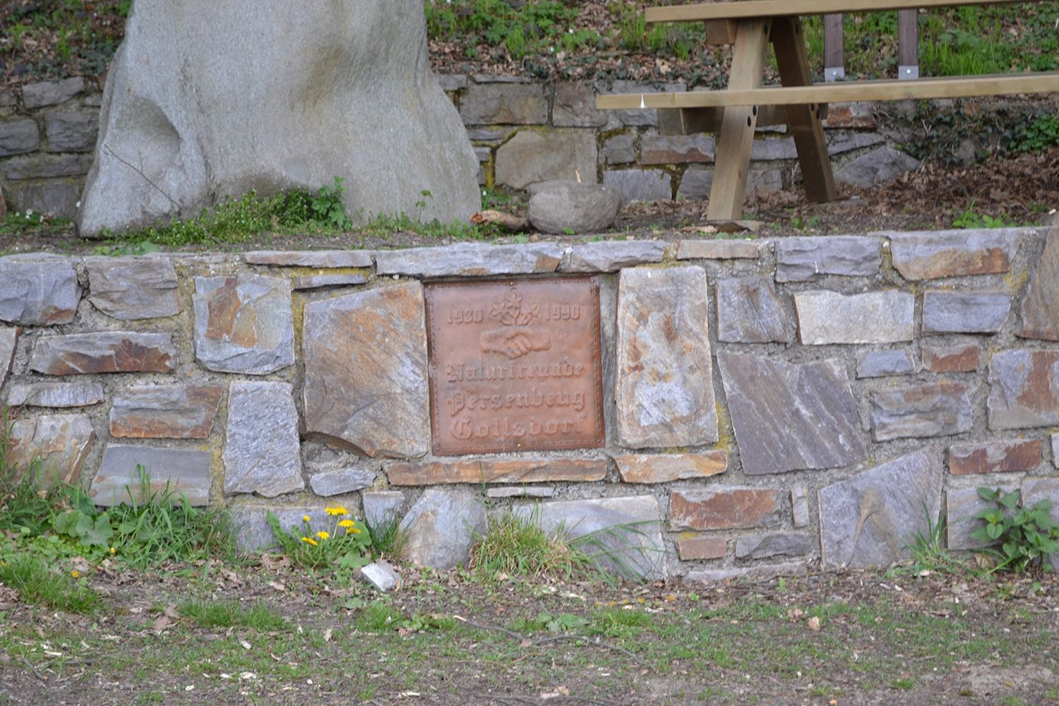 Stone wall with memorial plaque and picnic table in the background.