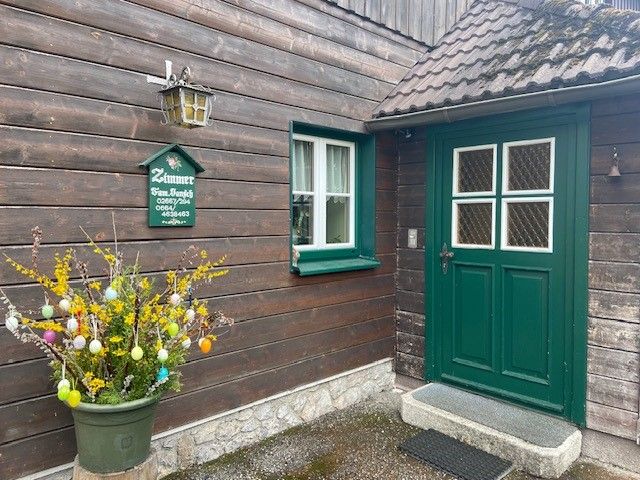Entrance of a wooden house with green door and window, decorated with an Easter shrub.