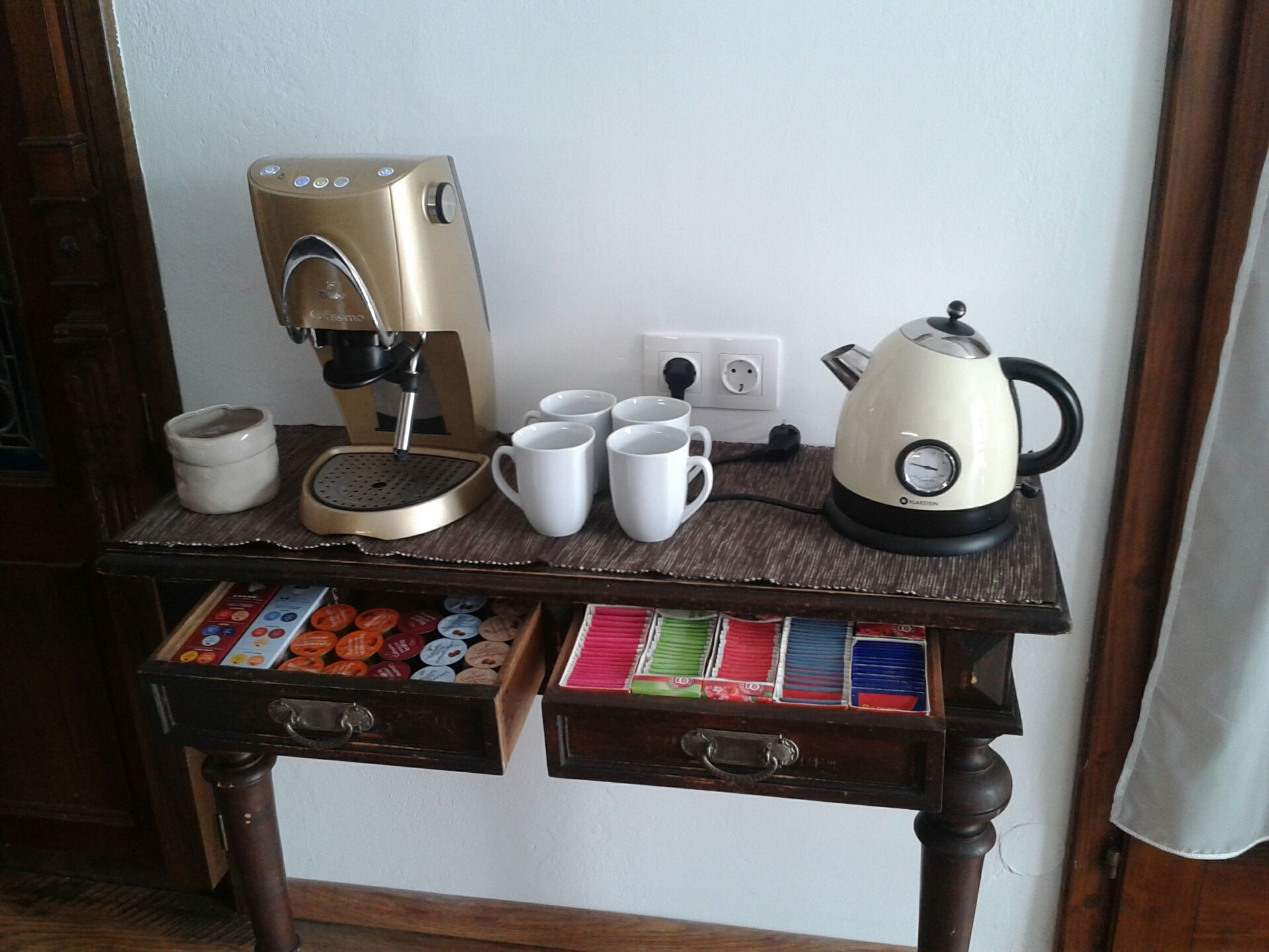 Coffee machine and kettle on a table with cups and tea bags.
