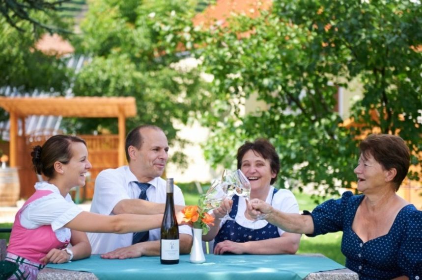 Four people clink glasses of wine at a table outside.