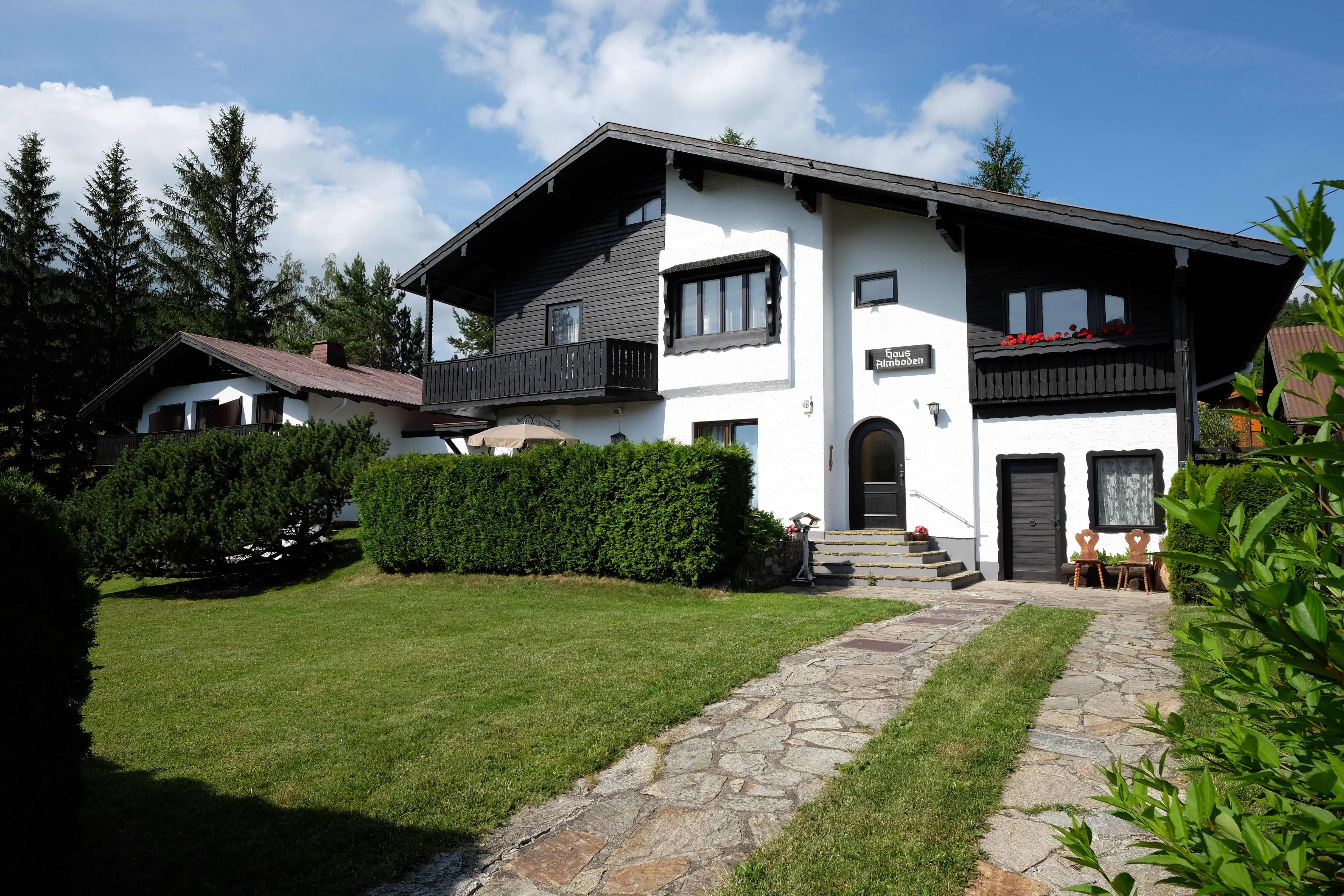 A two-storey house with black wood and white walls, surrounded by a well-tended garden and trees.
