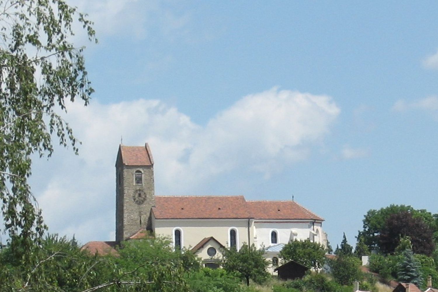 Church with tower and red roof in Hohenwarth, surrounded by trees and blue sky.