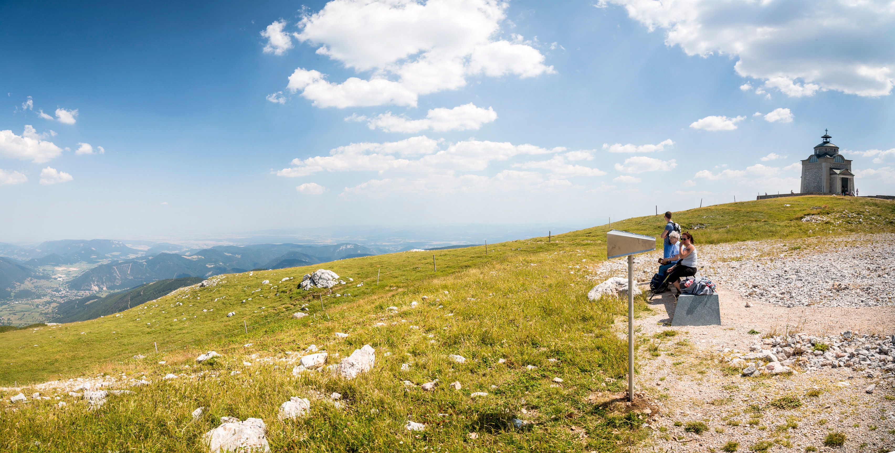 Panoramic view of the Elisabeth Church on the Schneeberg with hikers in the foreground.