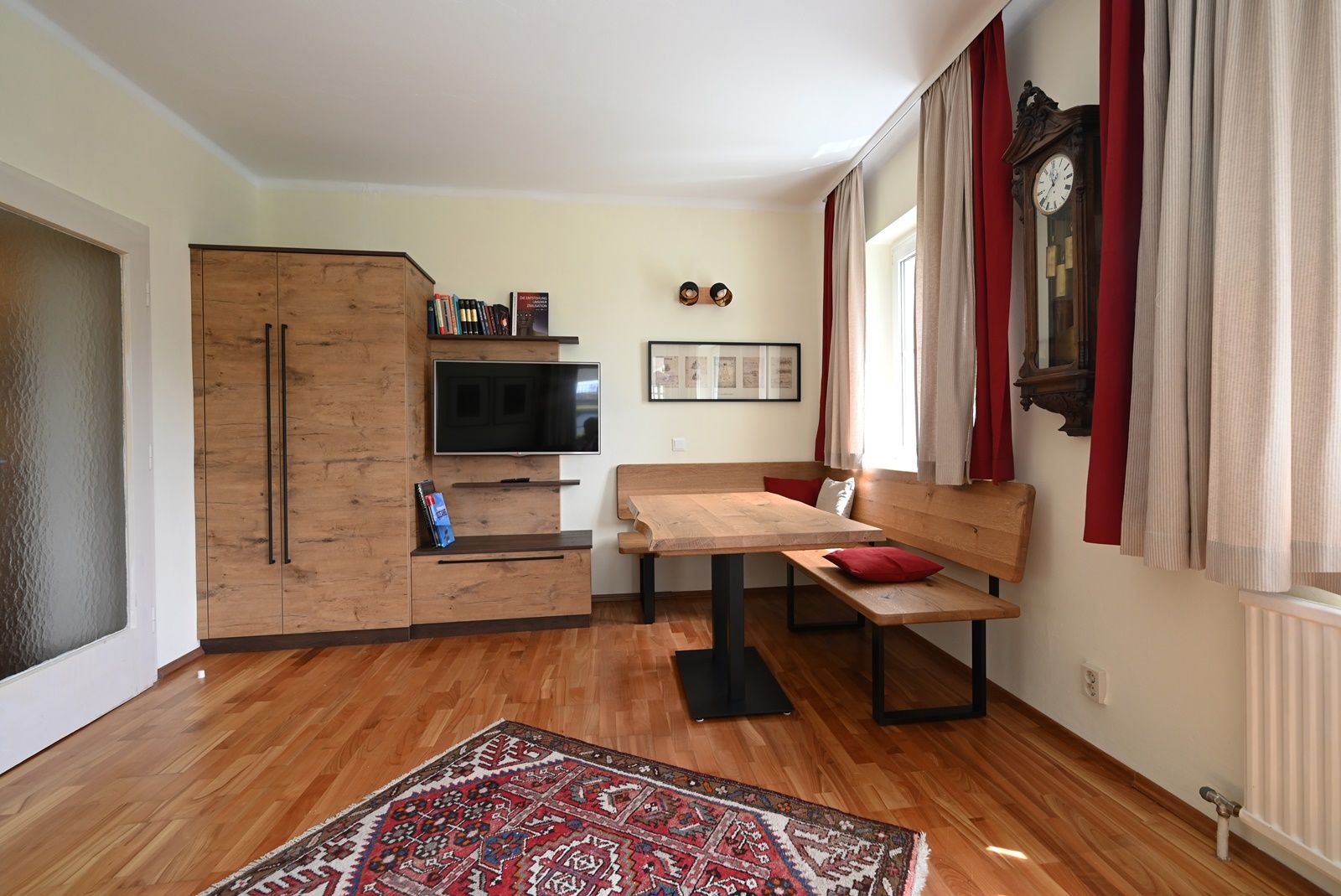 Cozy living room with wooden furniture, a carpet, a corner bench and a wall clock.