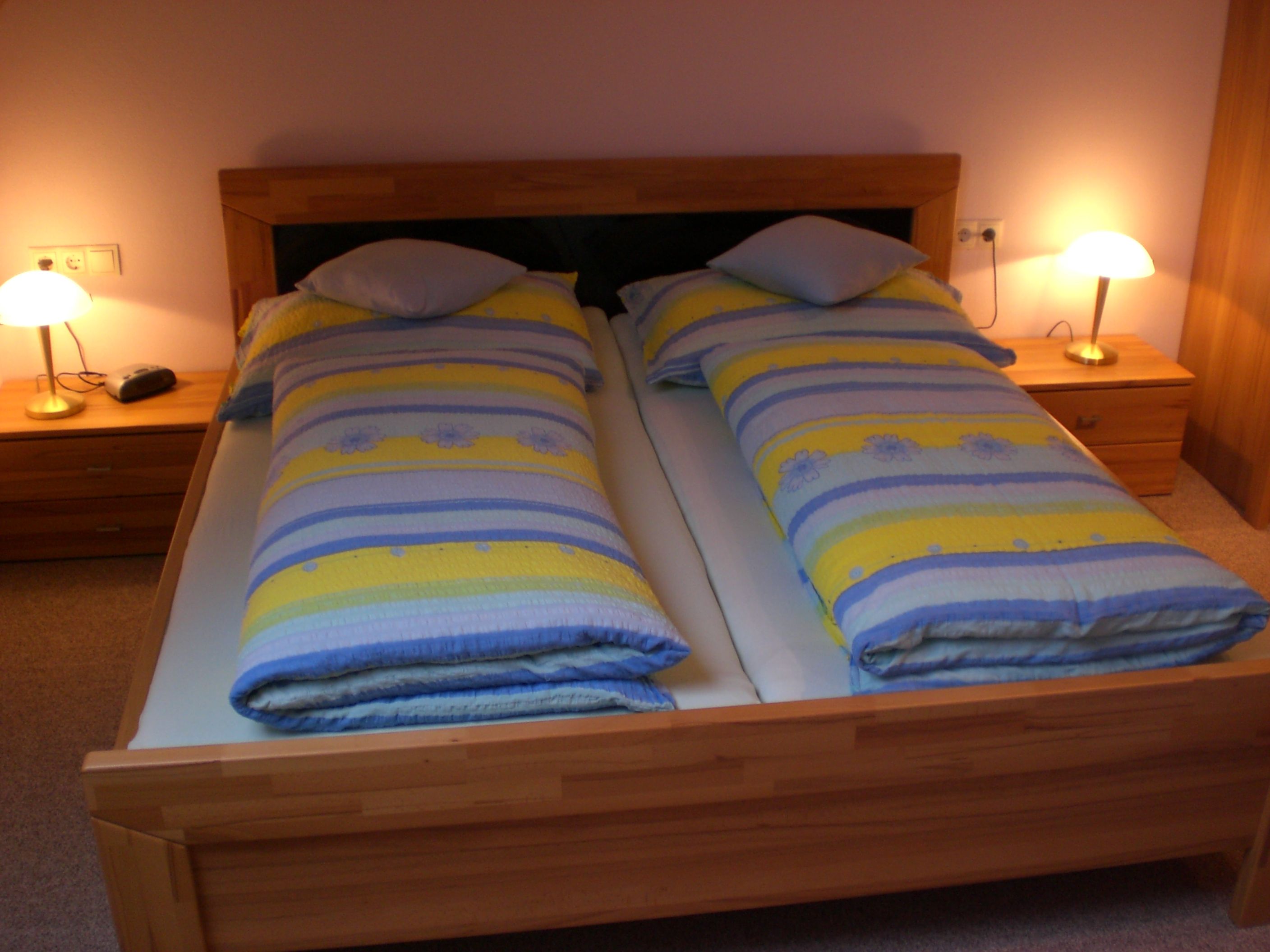 A cozy guest room with a double bed, colorful comforters and two bedside tables with lamps.