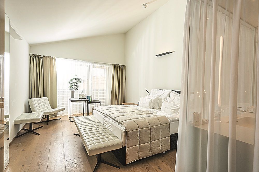 Modern hotel room with large bed, white furniture and wooden floor.
