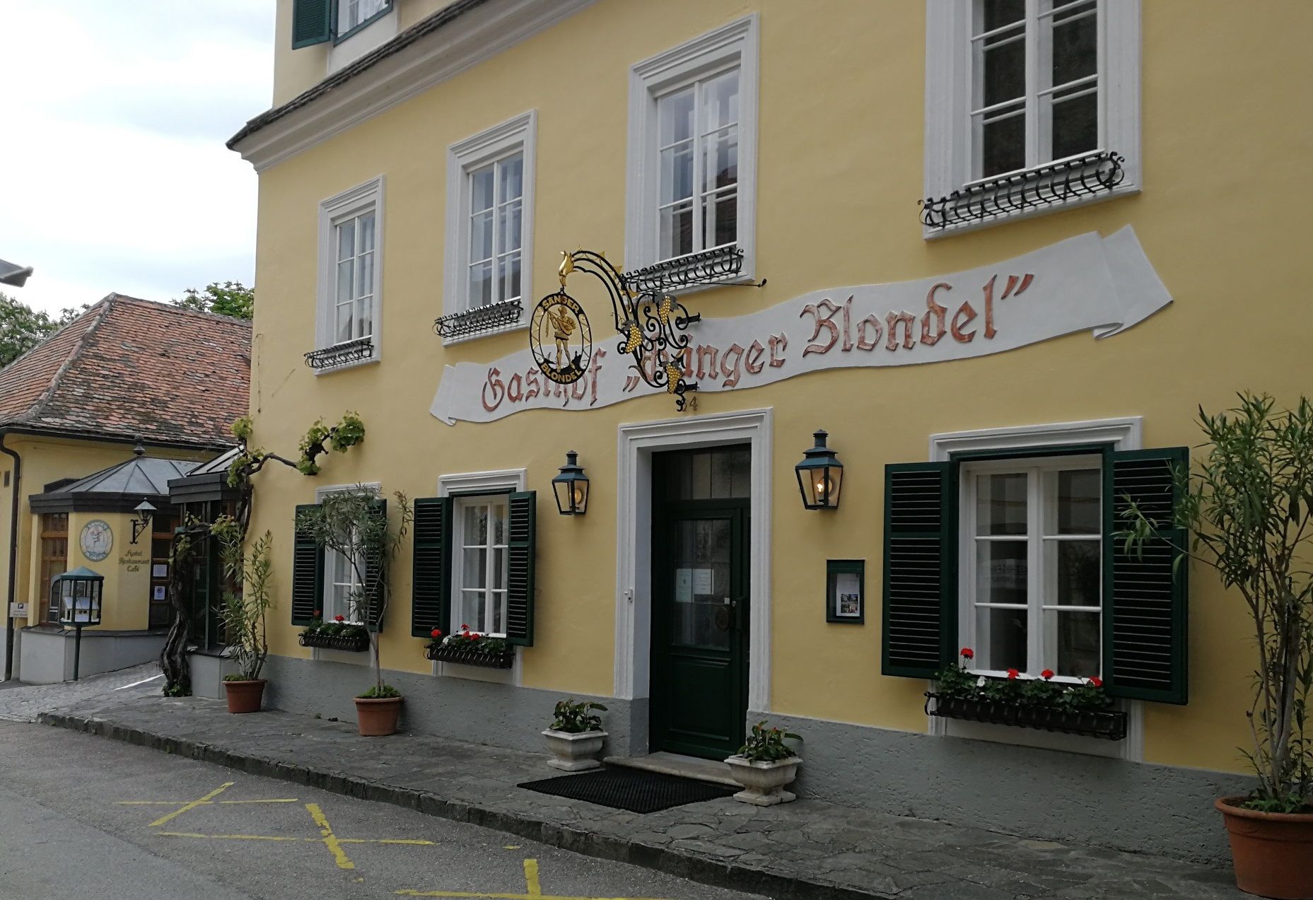 Yellow building with the inscription 'Gasthof Sänger Blondel', windows with green shutters and flower boxes.