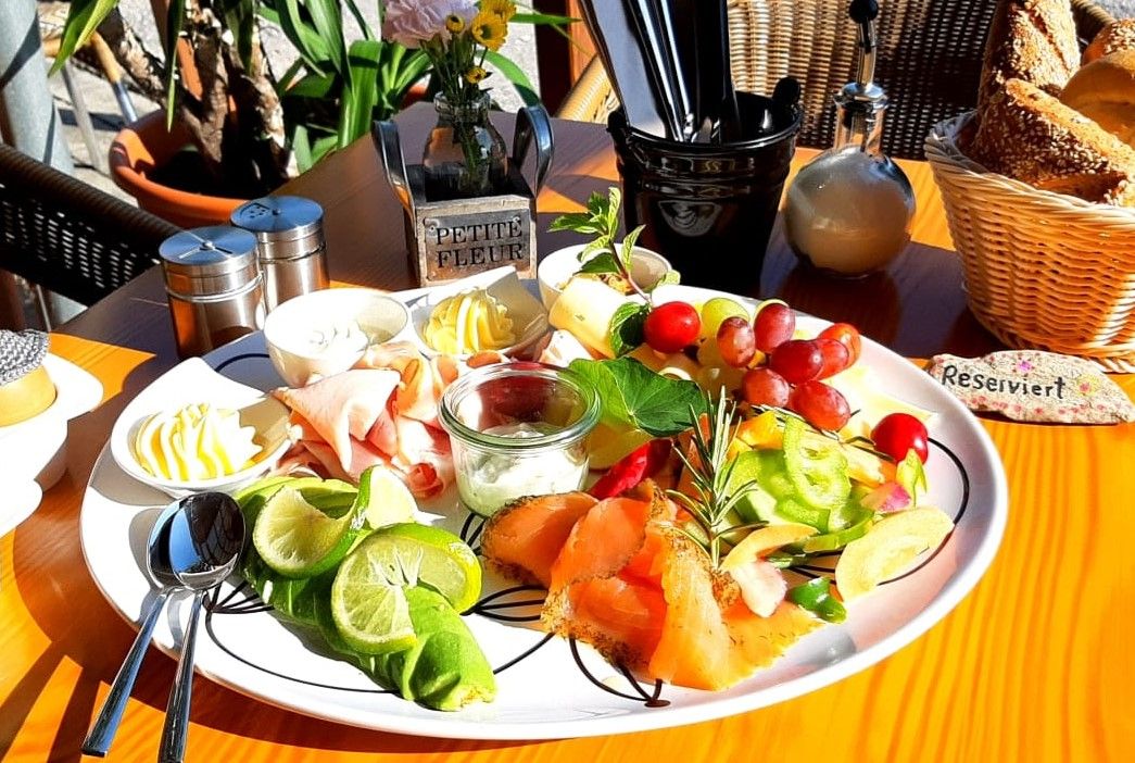 A breakfast plate with salmon, cold cuts, fruit and butter on an outdoor table.