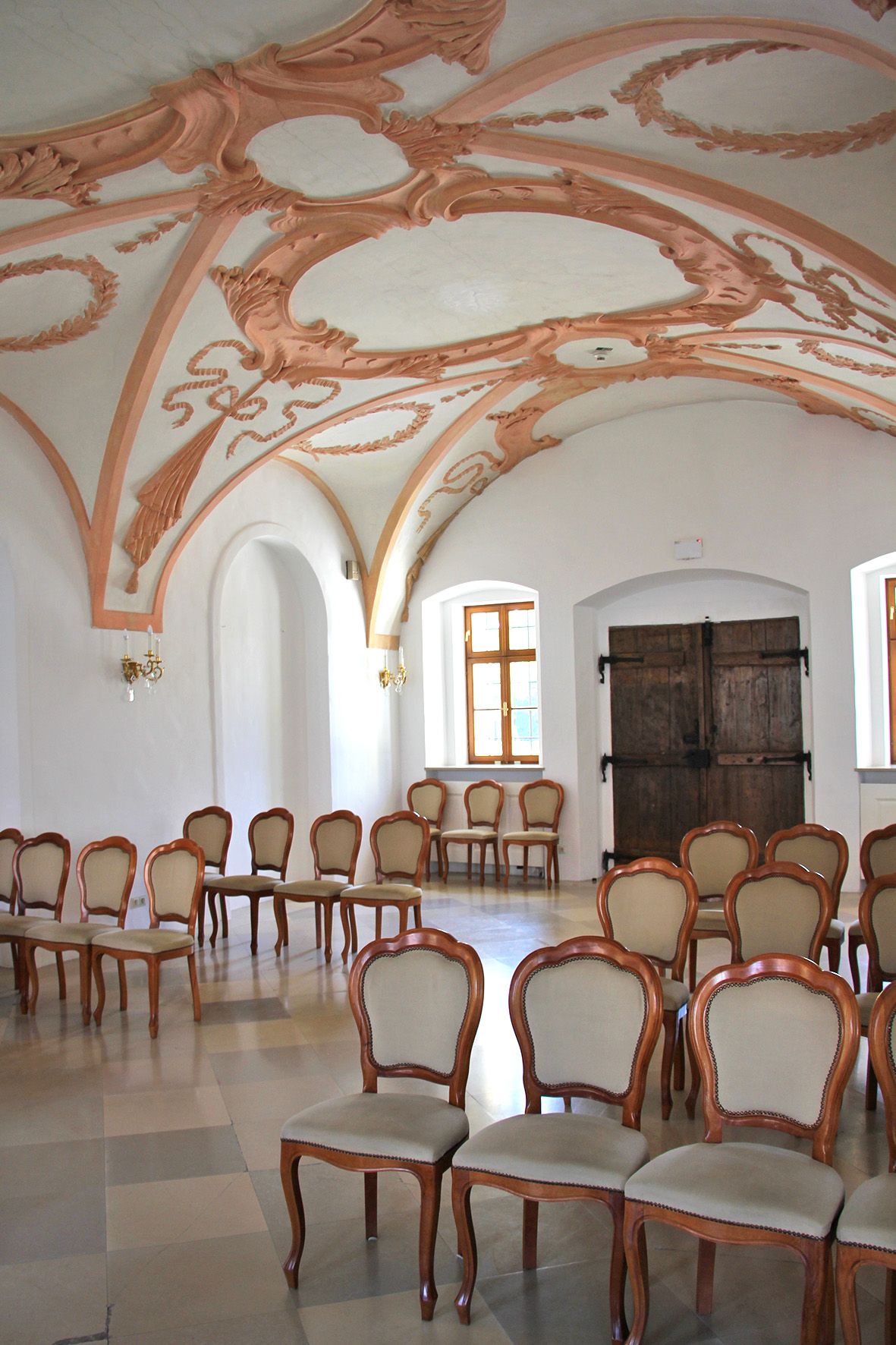 Interior view of a historic room with ornate stucco ceilings and elegant wooden chairs.