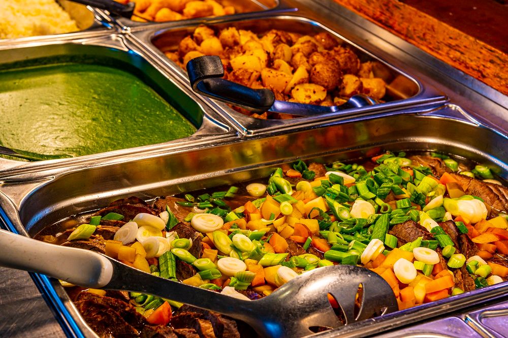 Buffet with various dishes in stainless steel containers.