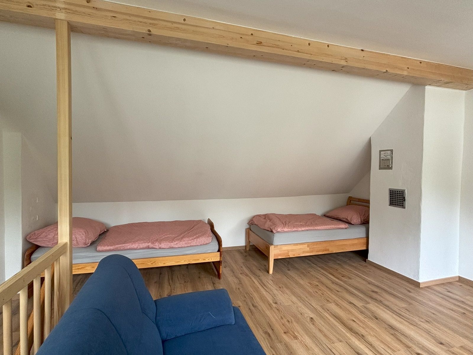 Two single beds with pink bed linen in a room with wooden floor and blue couch.