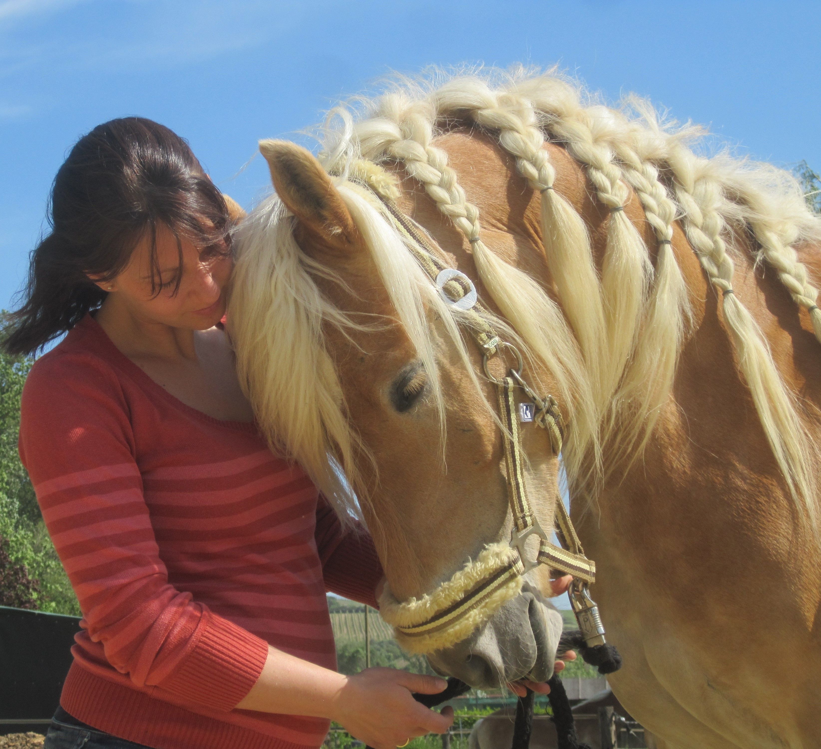 A woman in a red sweater stands next to a horse with a braided mane.