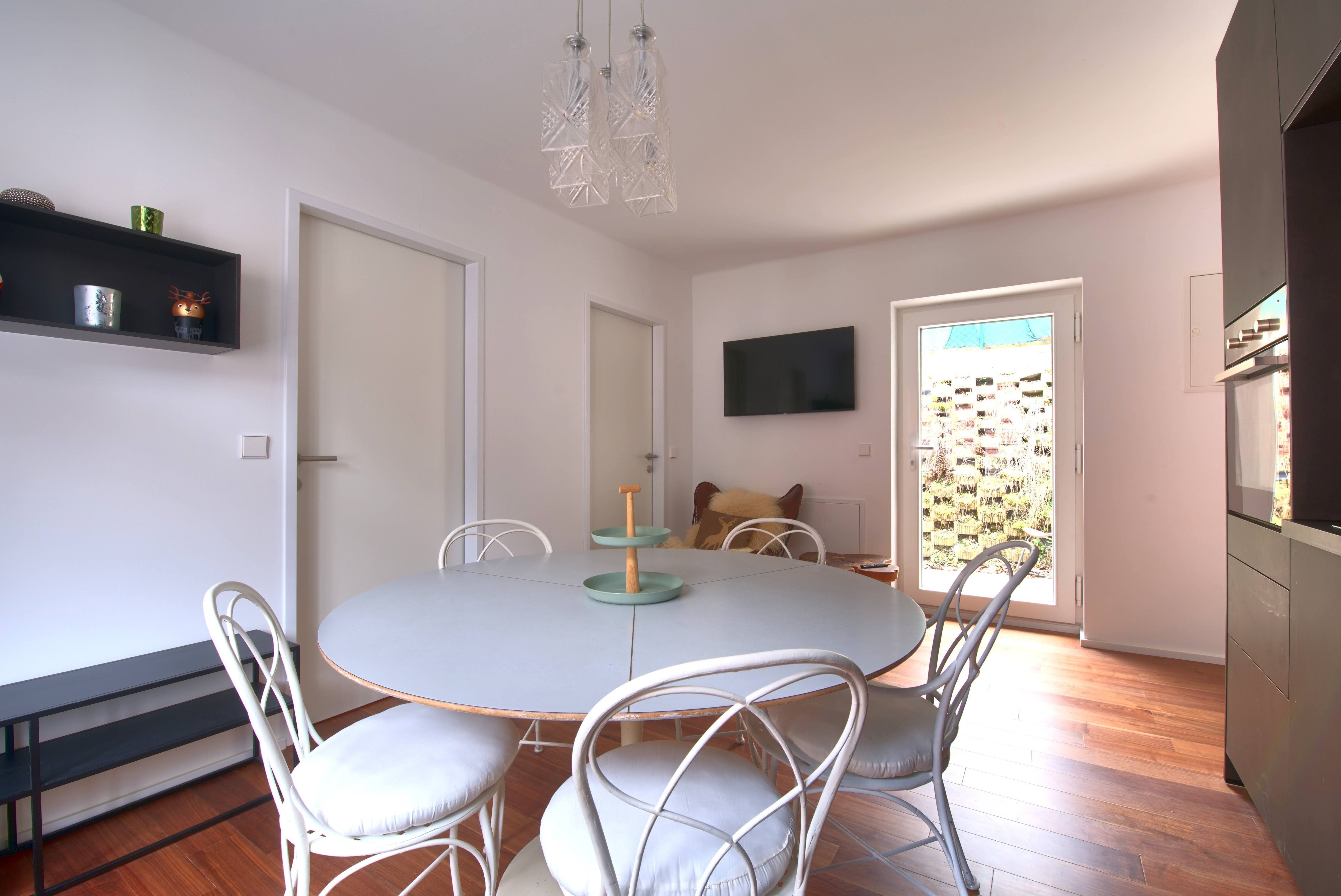 Modern dining area with round table, white chairs and wooden floor.