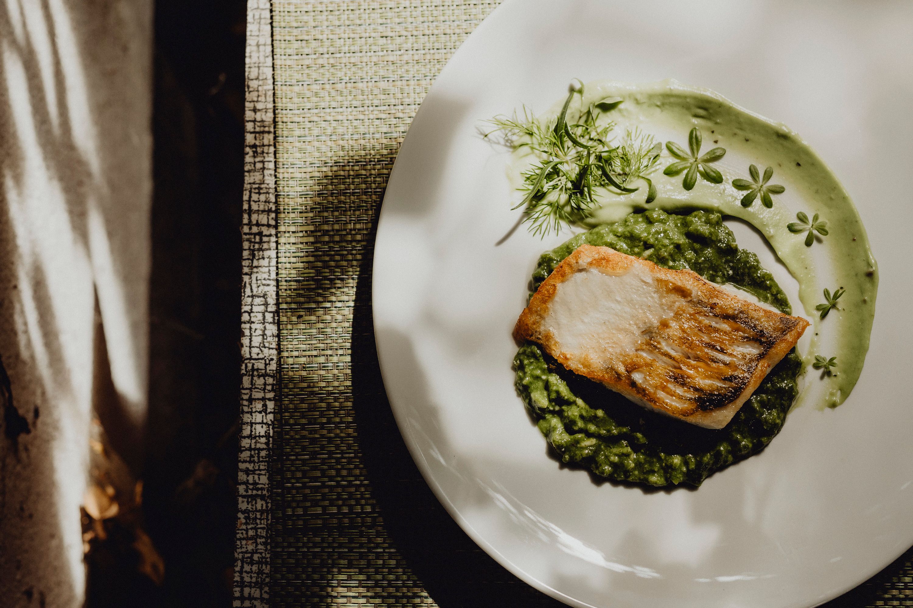 Pike-perch fillet on spinach risotto with basil cream on a white plate.