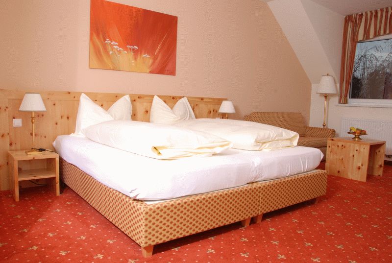 Comfortable hotel room with double bed, wooden furniture and red carpet.