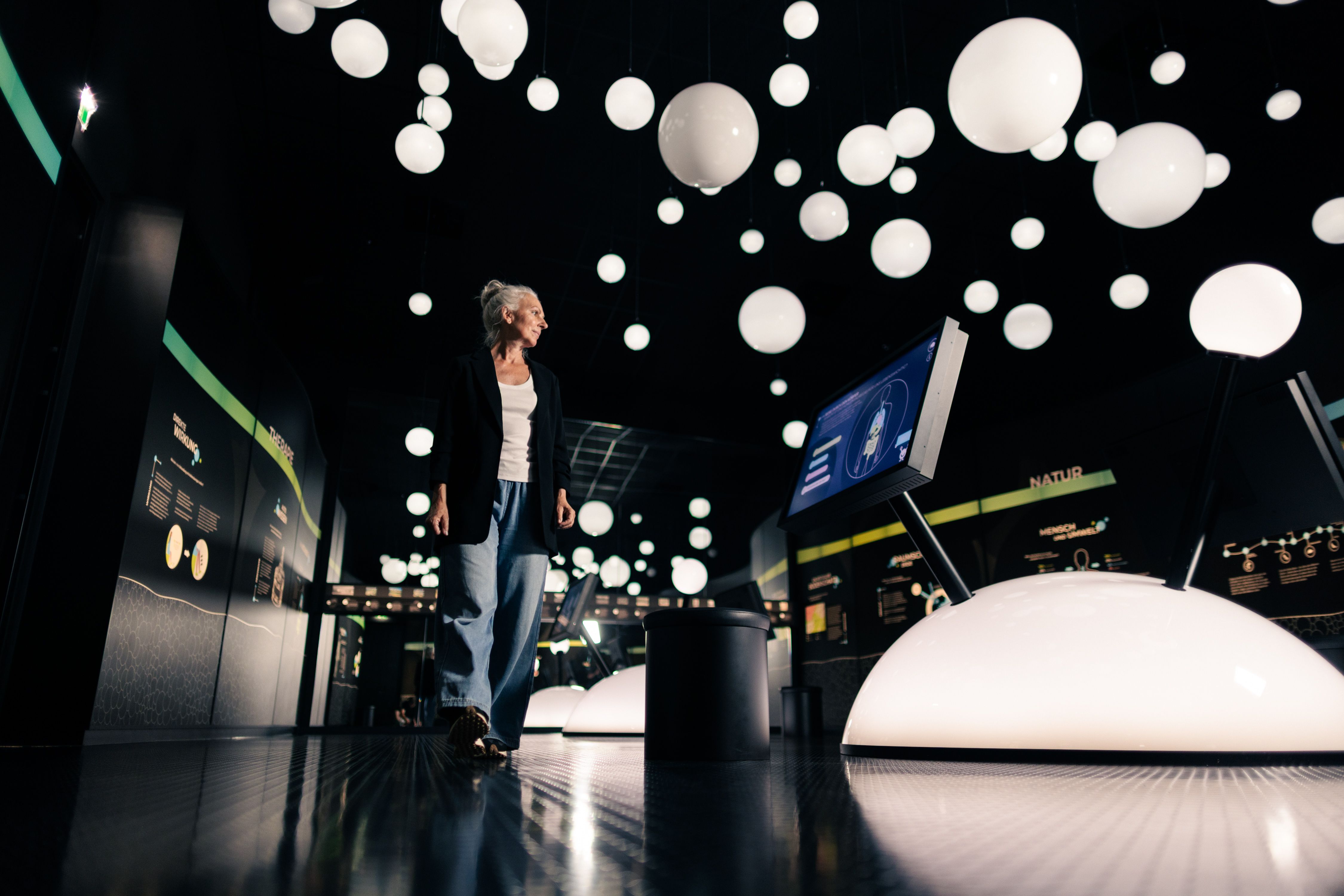 A woman is standing in a modern exhibition space with many glowing spheres hanging from the ceiling and interactive screens.