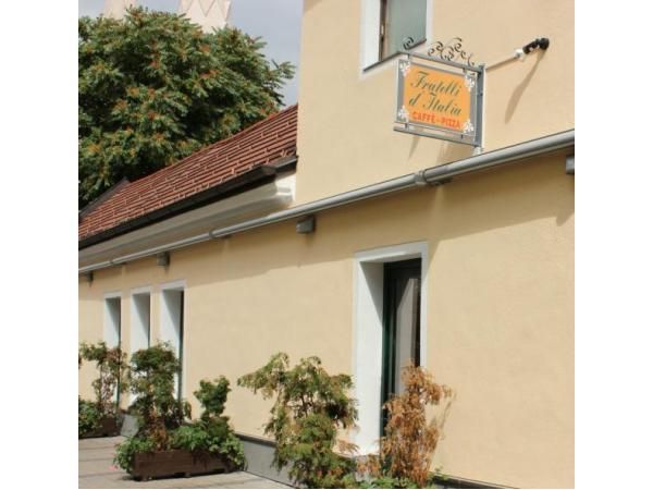 Exterior view of a yellow building with a sign "Fratelli d'Italia Caffè-Pizza" and plants in front of the façade.