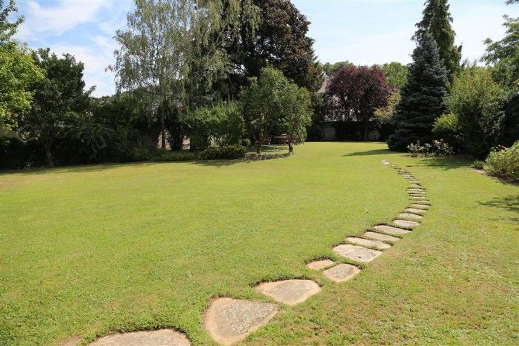 A well-kept garden with a curved stone path and trees in the background.