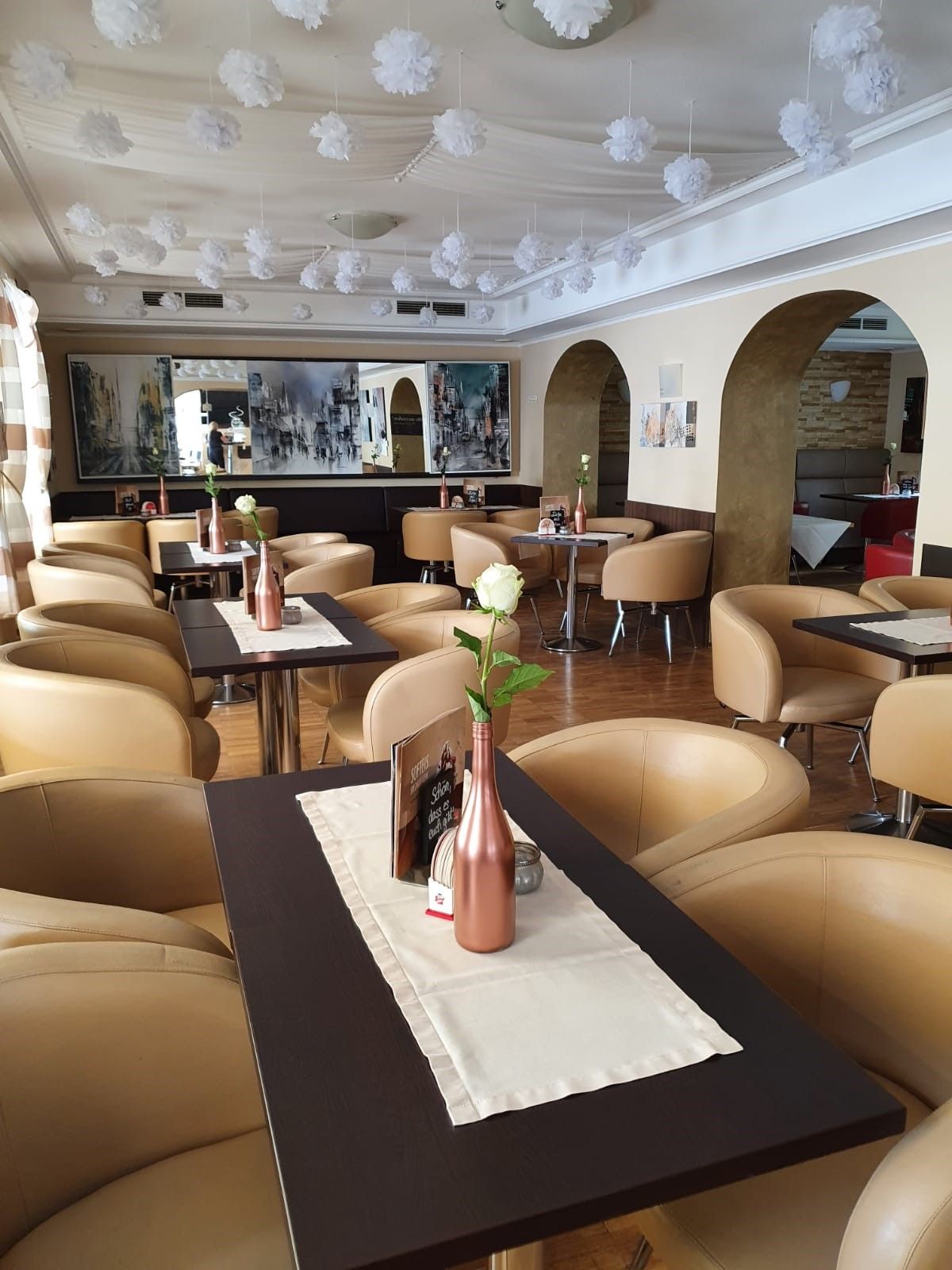 Interior view of a stylish café with beige armchairs and decorative white flowers on the ceiling.