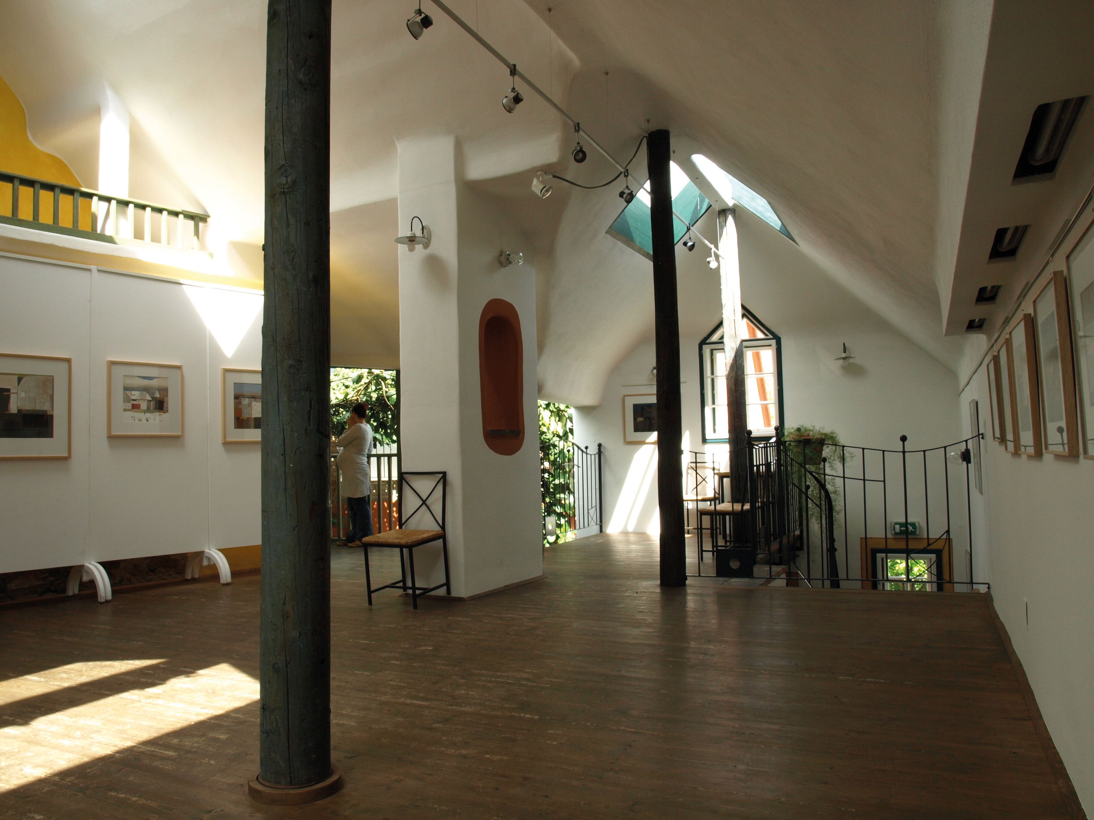 Interior view of a bright gallery with wooden floor, works of art on the walls and a person at the window.