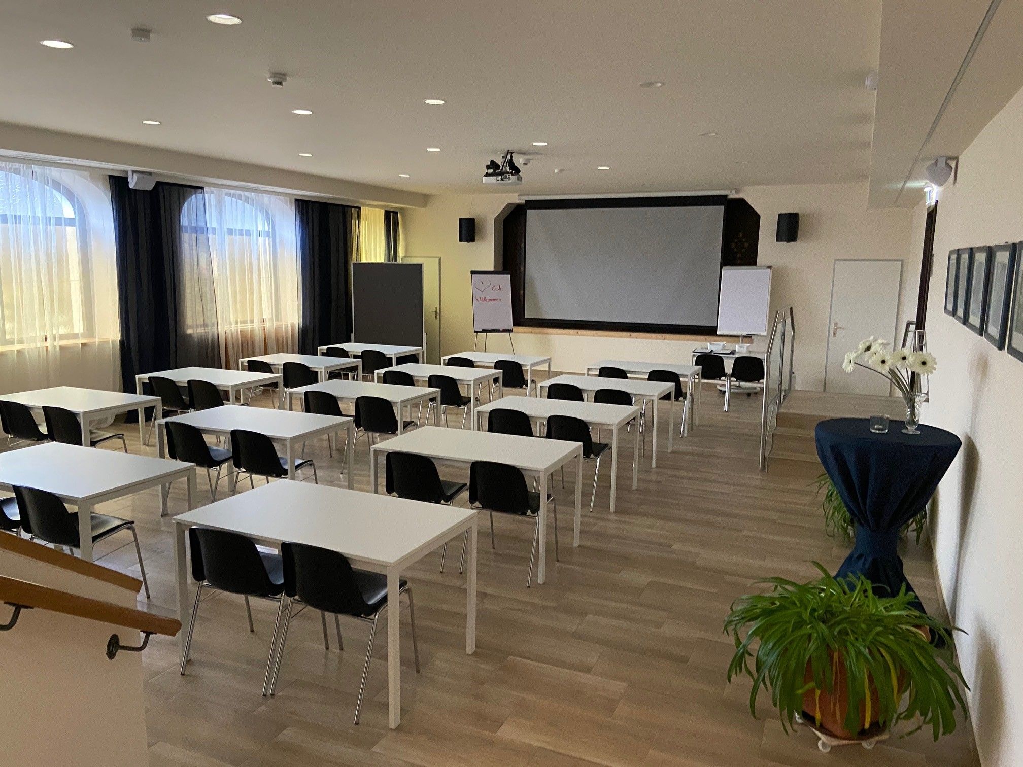 An empty seminar room with white tables, black chairs and a large screen at the front.
