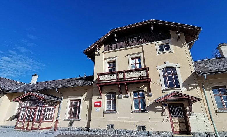 Historic station building with yellow façade and red wooden decor under a blue sky.
