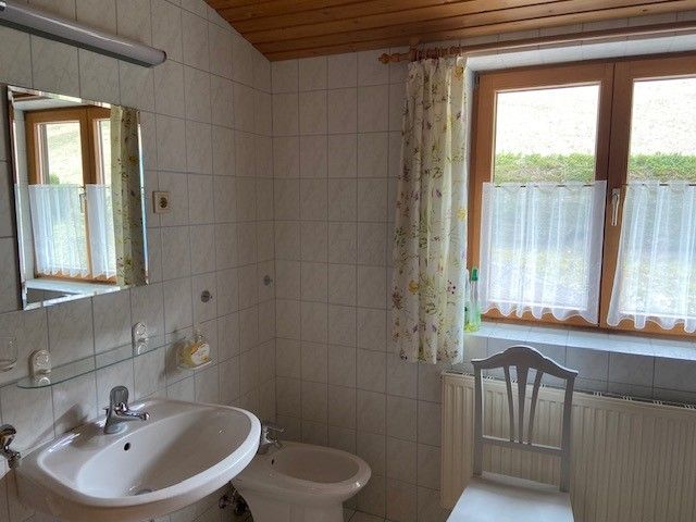 A bathroom with washbasin, bidet, mirror and window with curtains.