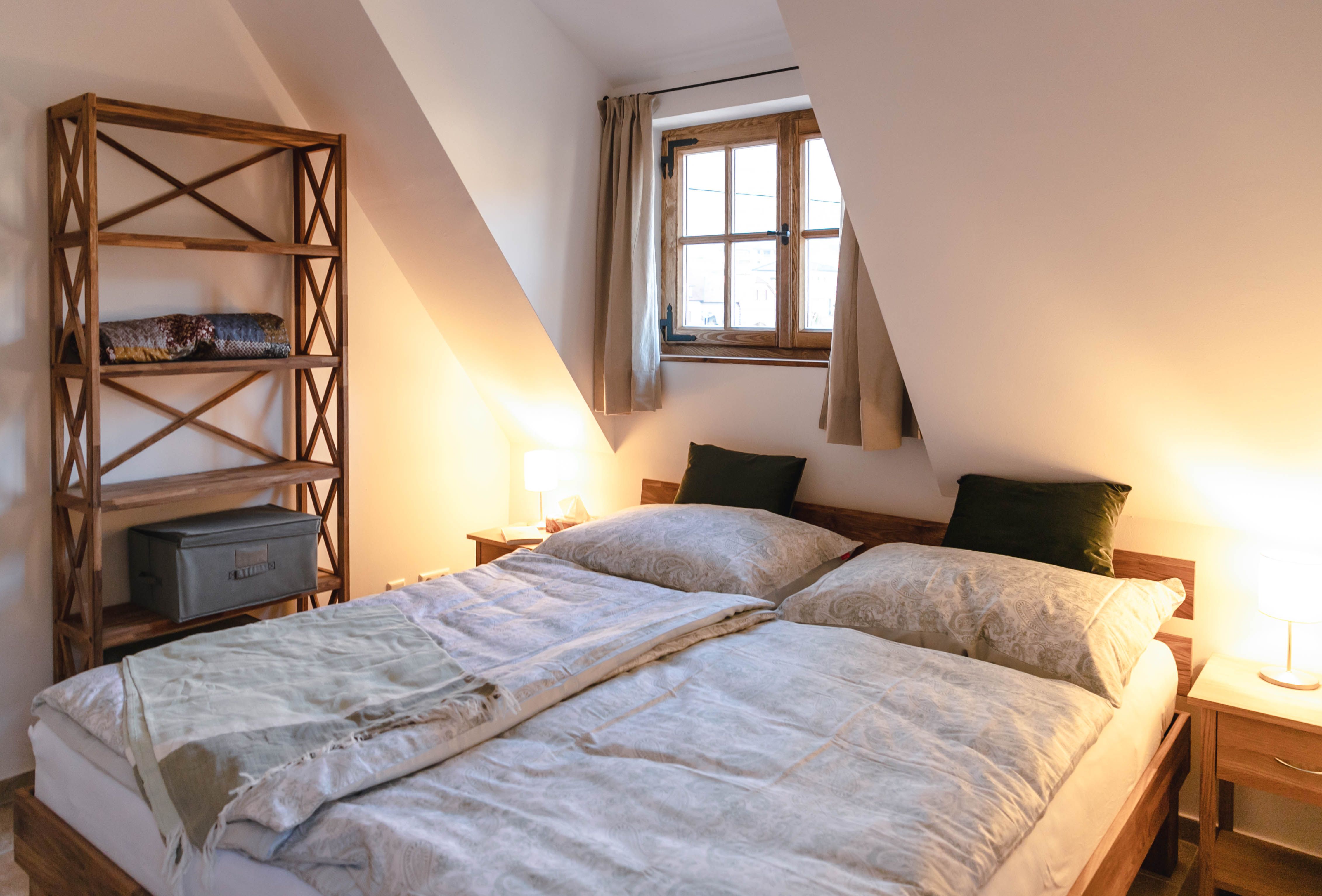 Cozy bedroom with double bed, wooden bookshelf and window with curtains.