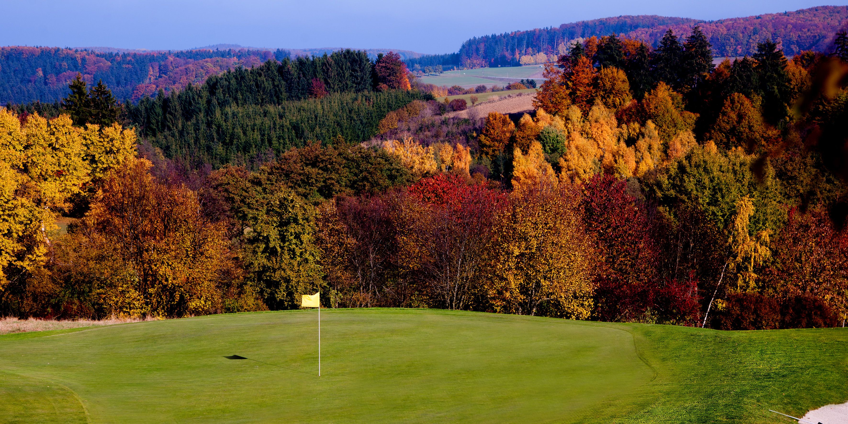 Golf course with fall trees in the background, yellow flag on the green.