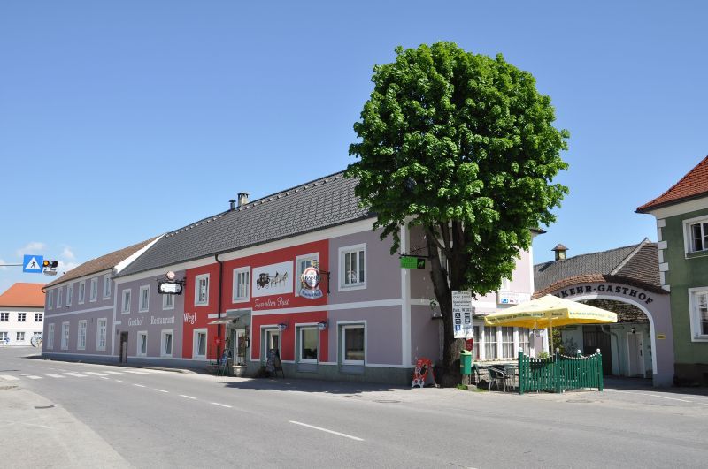 Gasthof Wegl on a street with a tree and sunshades.