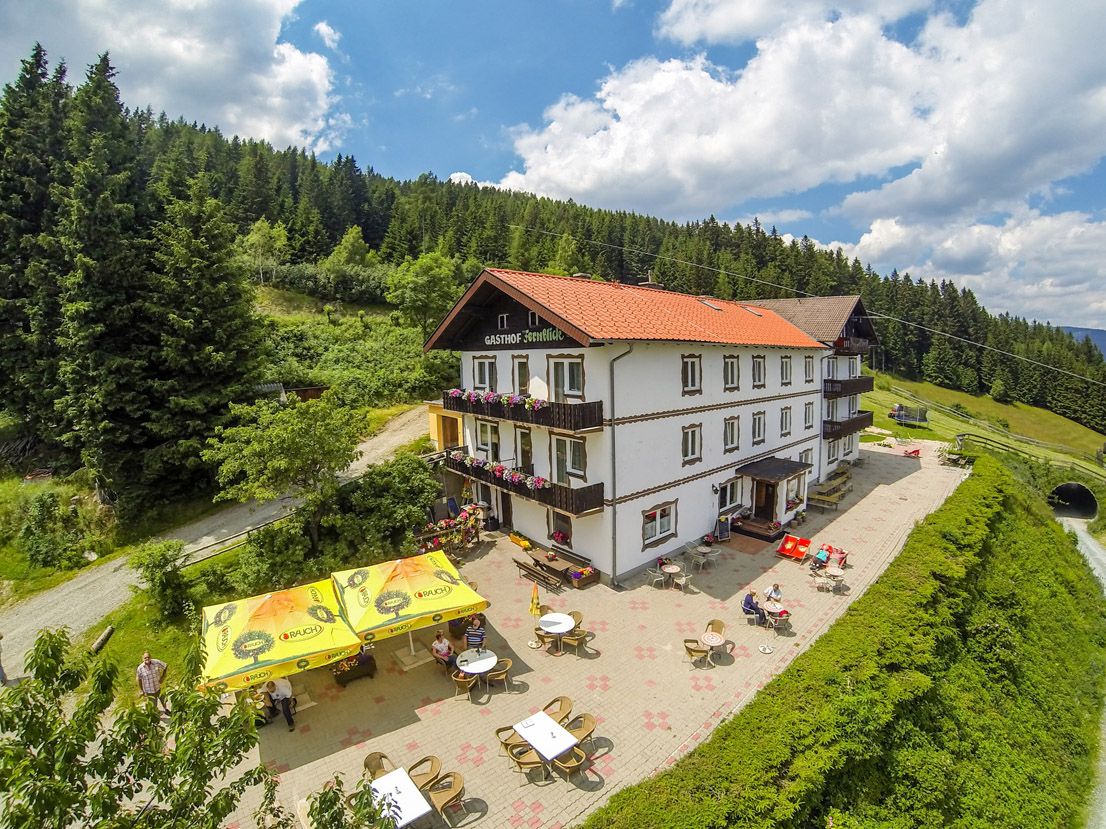 Alpine inn with terrace and sunshades in a mountainous landscape.