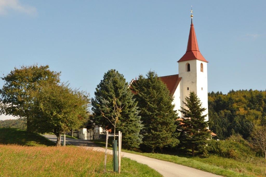Ofenbach parish church with red tower roof, surrounded by trees and meadows.