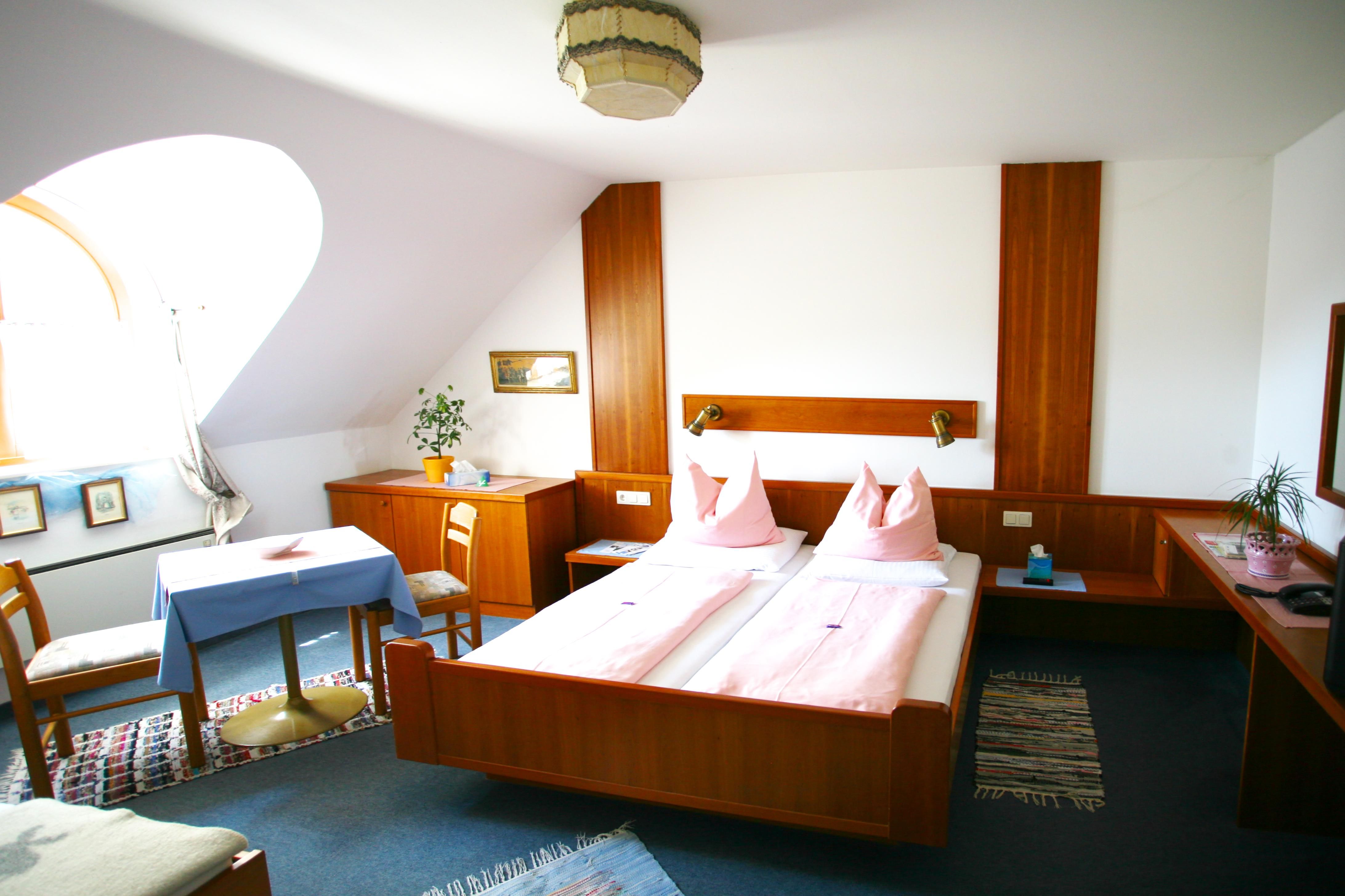Comfortable hotel room with double bed, wooden furniture and table with chairs.