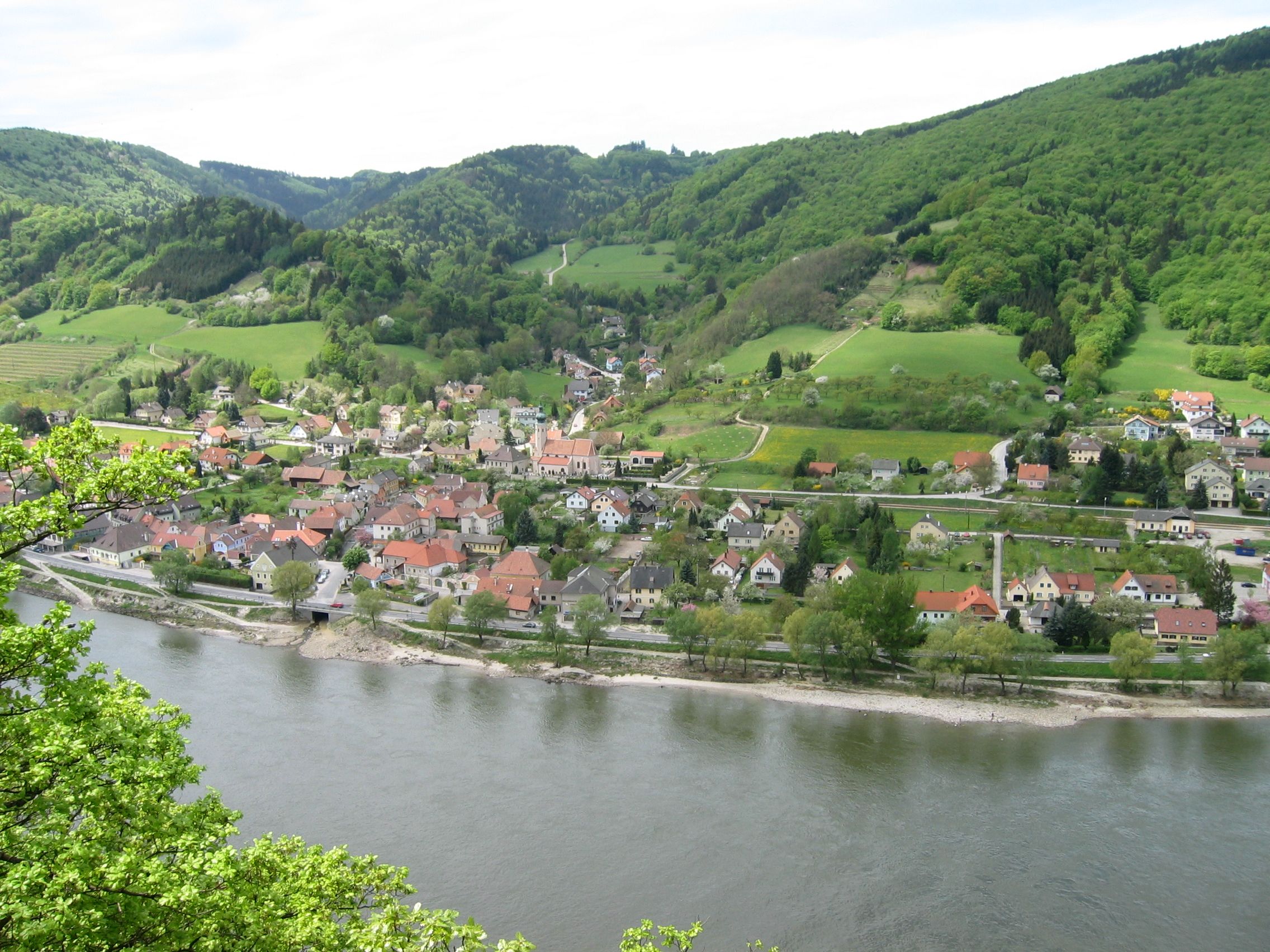 Aerial view of Aggsbach with river and green hills in the background.