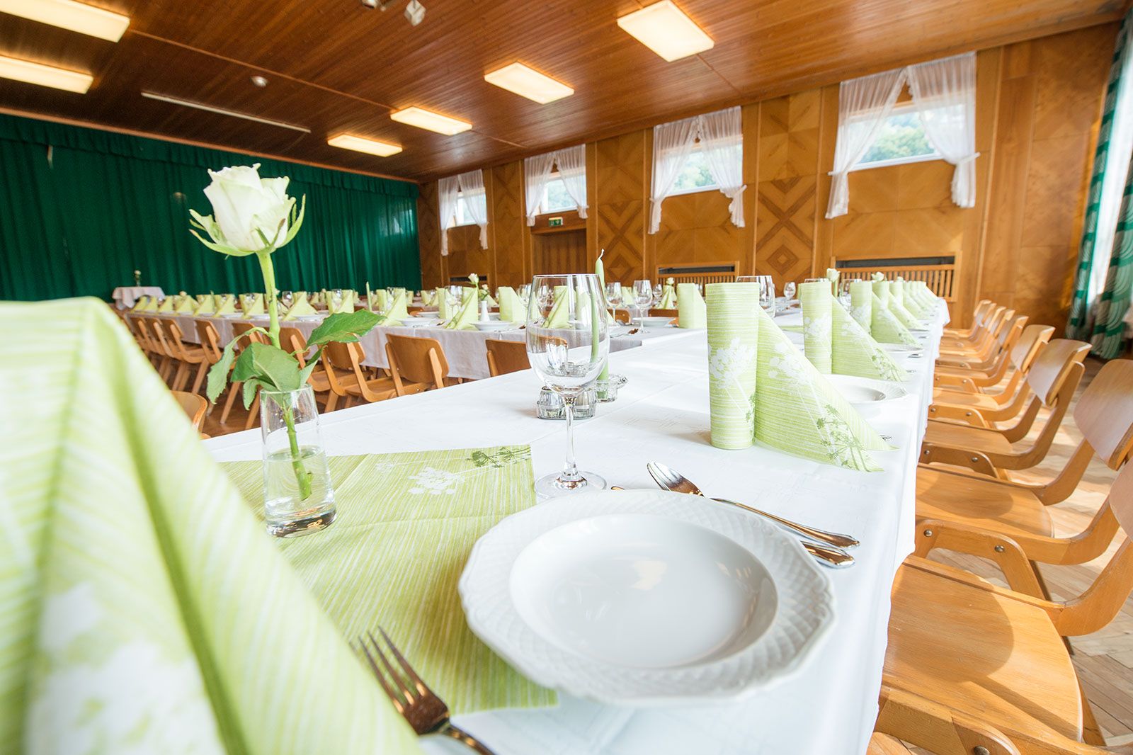 Festively decorated hall with long tables, green napkins and white roses.