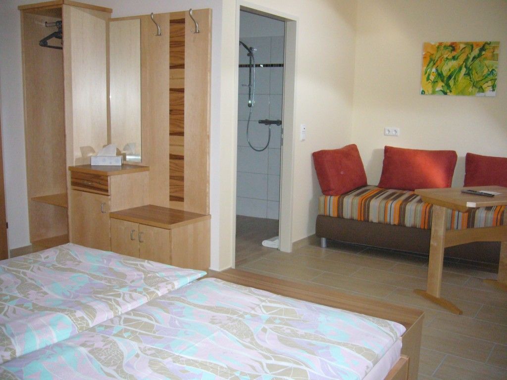 A cozy double room with two beds, a wardrobe, a small table and a couch. A bathroom can be seen in the background.