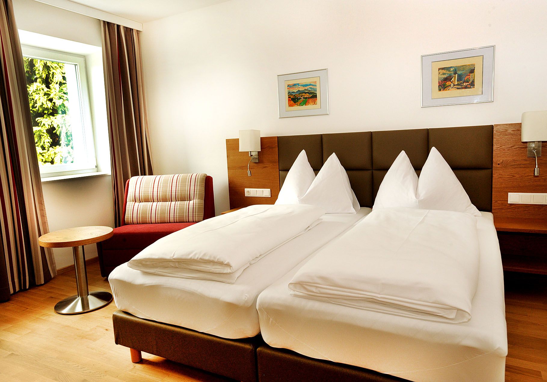 A modern hotel room with a double bed, armchair, small table and two pictures on the wall.