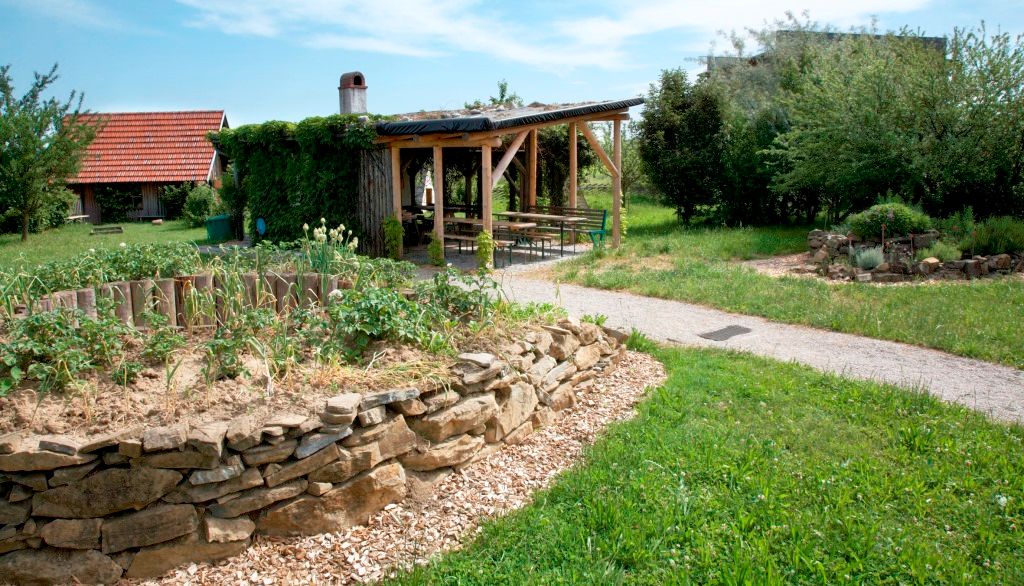 A garden with a raised stone bed, covered seating area and lawn.