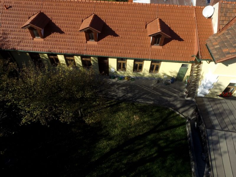 Aerial view of a building with a red tiled roof and several windows, surrounded by a garden.