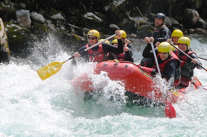 Group rafting on a river with yellow helmets and red vests.
