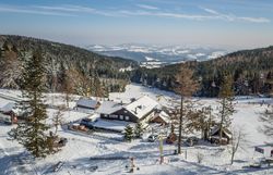Ski area with chair lift and skiers, surrounded by snow-covered trees and hills.