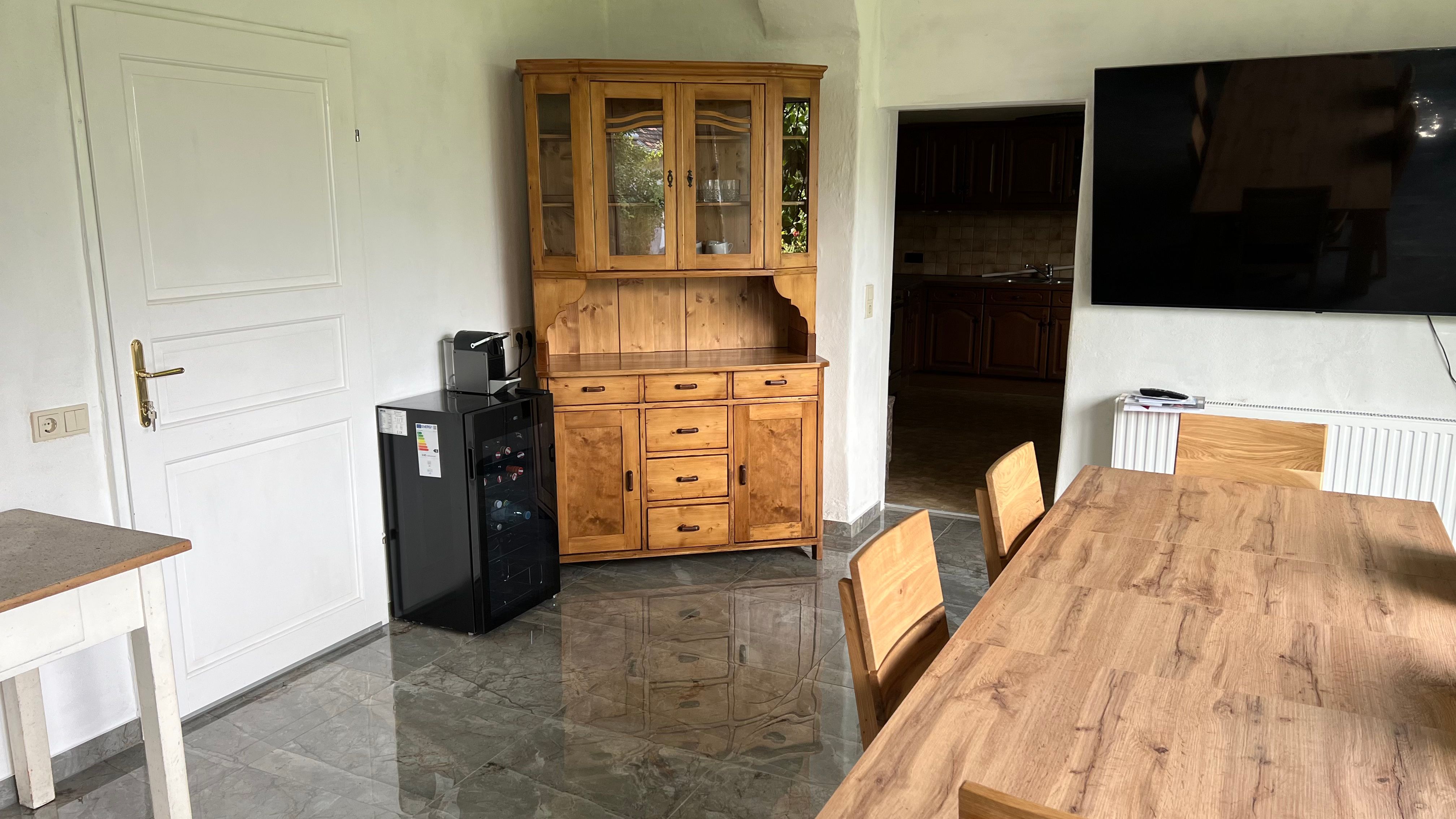 Dining room with wooden table, chairs, display cabinet, fridge and large TV on the wall.