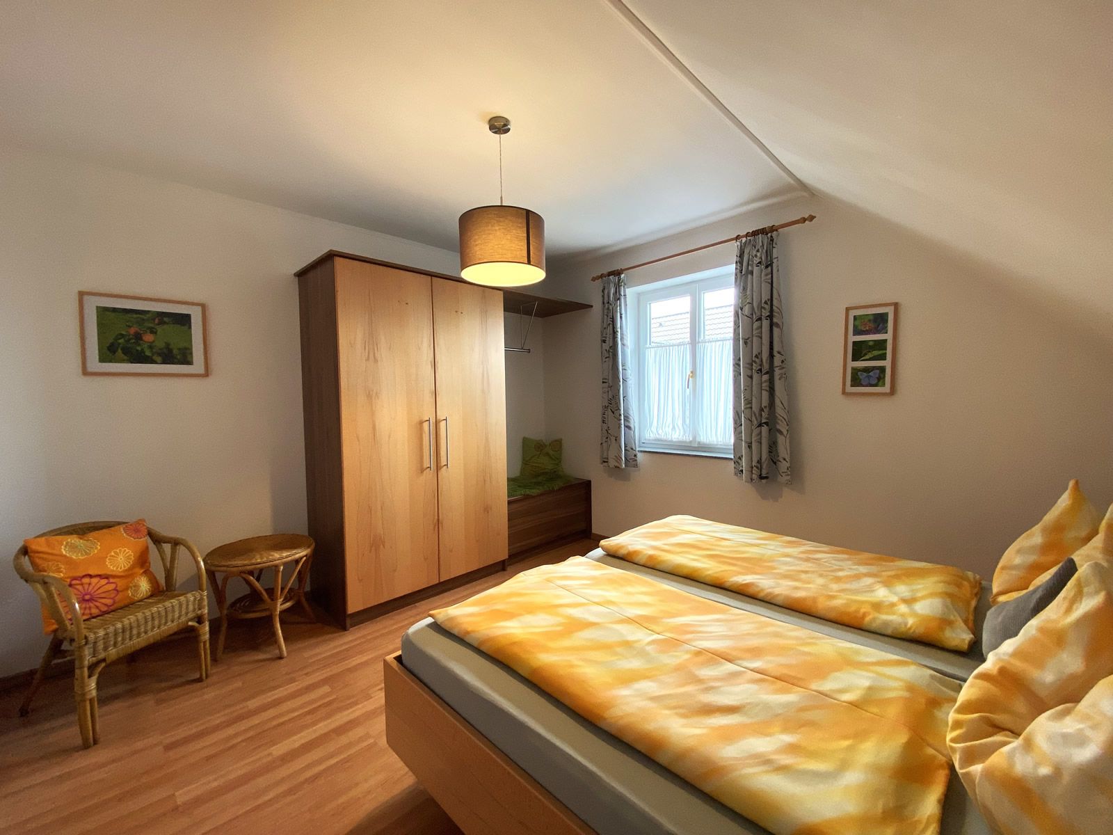 Bedroom with double bed, wooden wardrobe, wicker chair and window with curtains.