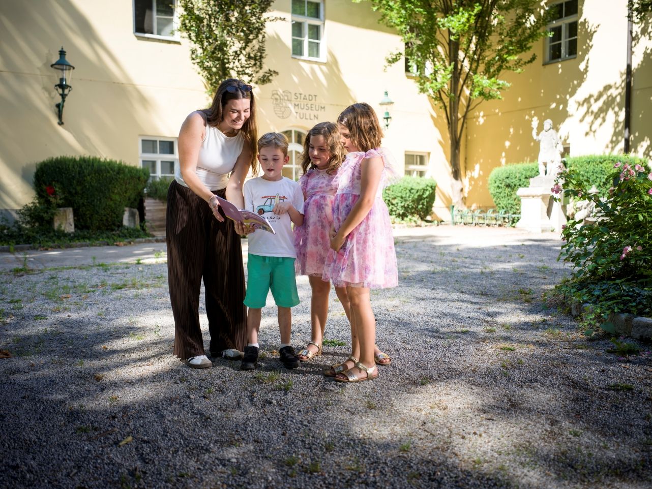 A woman and three children are standing in front of the Tulln City Museum, reading the brochure