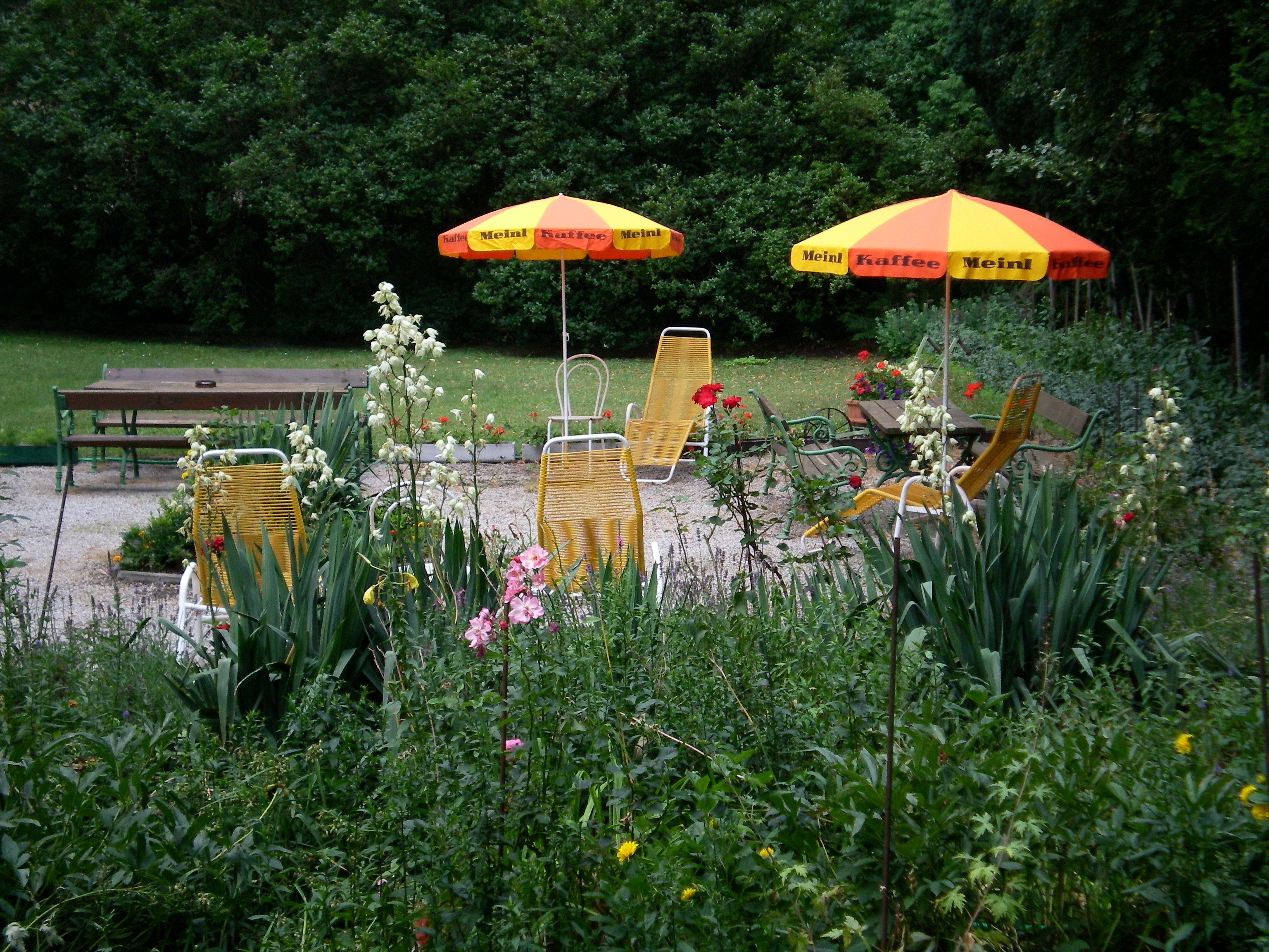 Garden with yellow sun loungers and parasols, surrounded by flowers and trees.