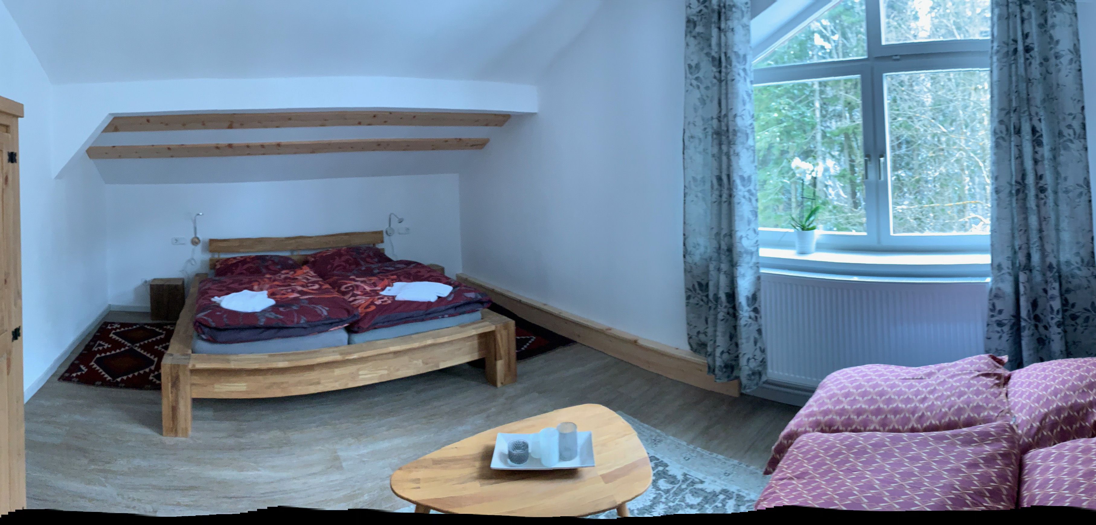 Cozy bedroom with wooden bed, sofa and large window with curtains.