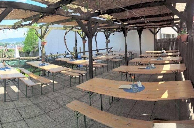 Empty wine tavern terrace with wooden benches and tables under a pergola.