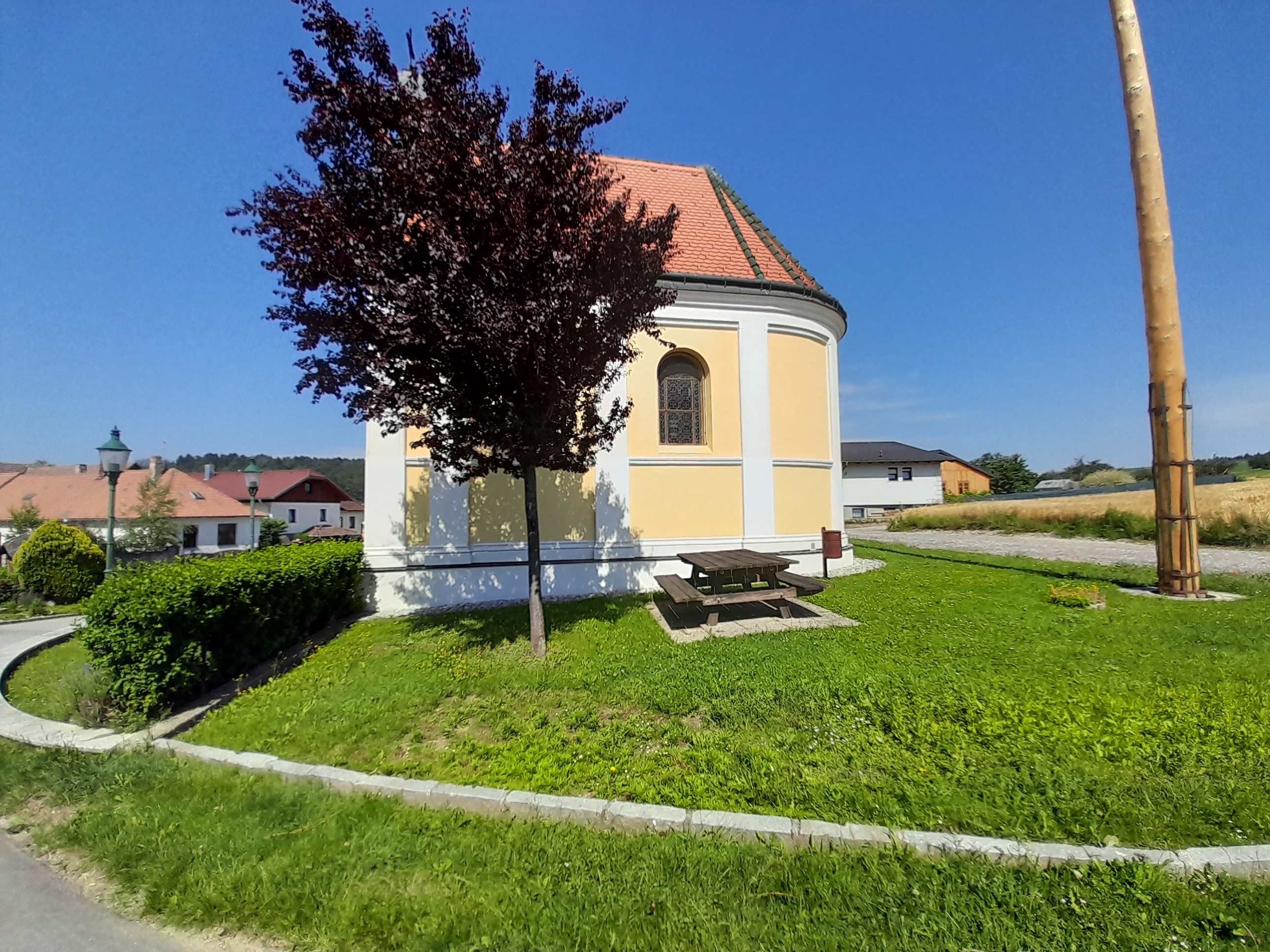 Round church with yellow façade, surrounded by green meadow and trees, in sunny weather.