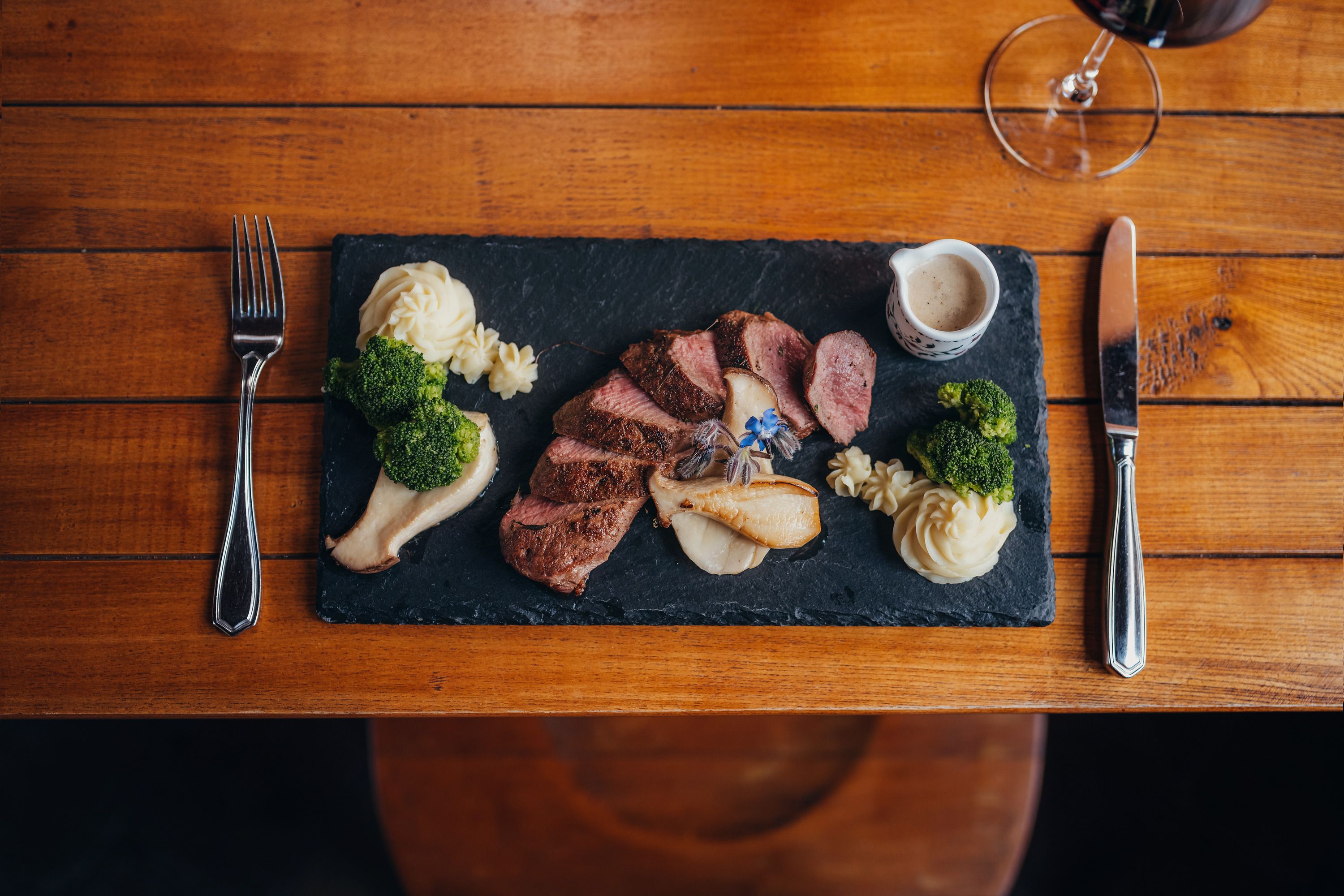 Gourmet dish on a slate with meat, puree, broccoli and sauce.
